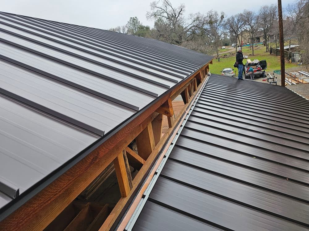 Metal roof installation on a residential building with workers and tools visible.